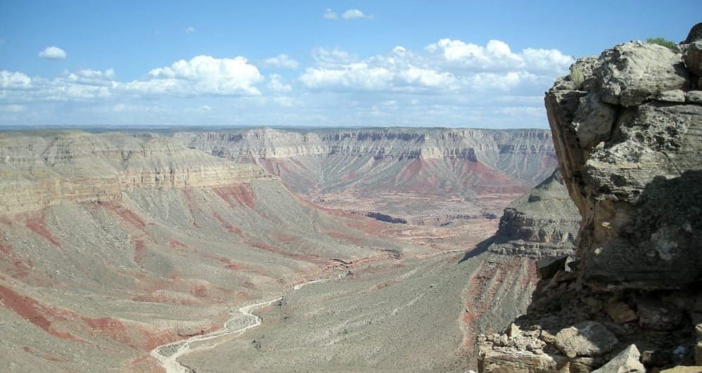 A large canyon dominates a landscape photo with a boulder in the foreground and partly cloudy skies are above.